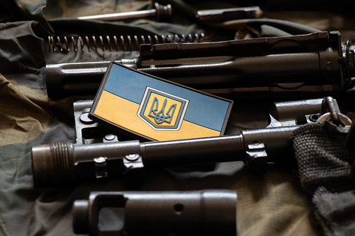The patch of the flag of Ukraine lies on a disassembled machine gun on a green camouflage fabric, war in Ukraine, military weapons