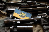 The patch of the flag of Ukraine lies on a disassembled machine gun on a green camouflage fabric, war in Ukraine