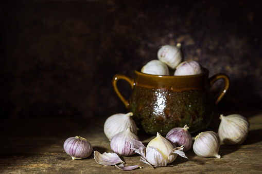 Fresh Single Clove Garlics or pearl garlic or solo garlic, variety of Allium ampeloprasum with a spice pot on dark background - dark and moody