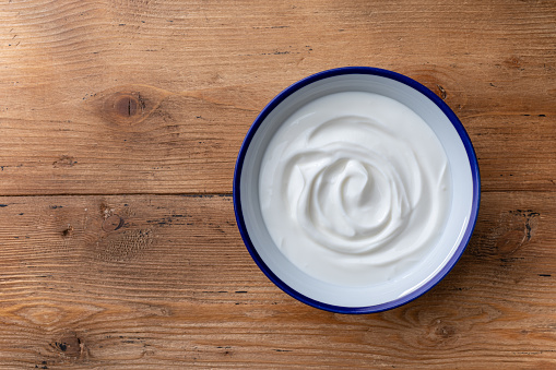 Greek yogurt in bowl on wooden rustic table top view and closeup.