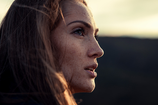 Close up side portrait of a woman with freckles during sunset.
