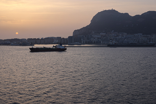 Gibraltar - June 16, 2022: Lone ship sits in the port of Gibraltar as dawn breaks over the Rock of Gibraltar