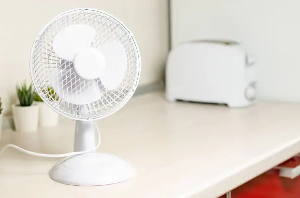 Photo of A small fan on the kitchen table. The concept of cooling and ventilation of the house.