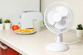 A small fan on the kitchen table. The concept of cooling and ventilation of the house.