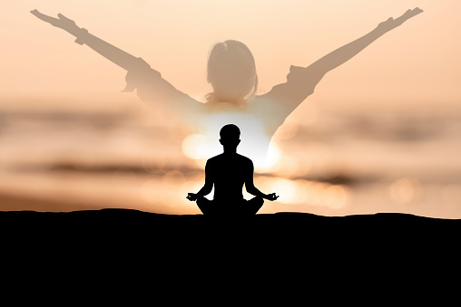 Silhouette of young male sitting practices yoga and meditating in lotus position alone on the beach with natural sunlight in the morning. He felt calm and happy.
