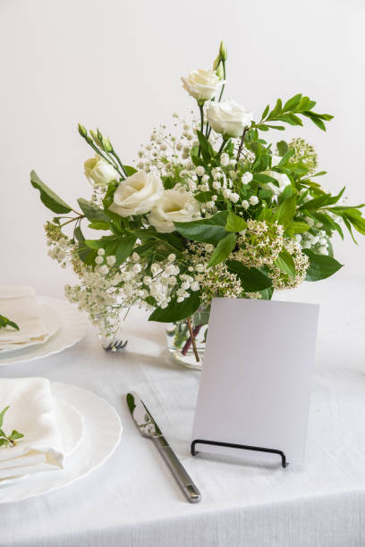 istock Mockup white blank space card for table number or menu. Wedding teble decoration with white flowers, glasses and white napkins. Elegantly decorated table at a wedding reception. Festive table setting. The wedding decor. 1404145150