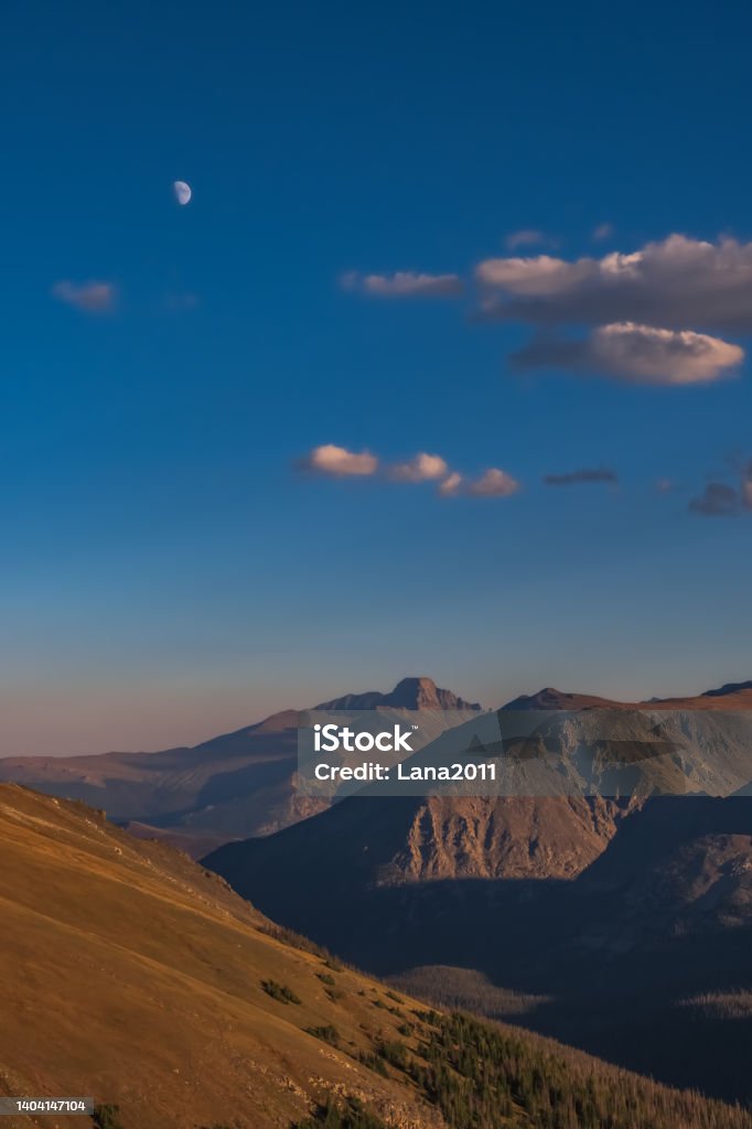 Vertical view of bare mountain peaks about tree line as seen from trail ridge road in Rocky Mountain National Park, Colorado, at sunset Vertical view of bare mountain peaks about tree line as seen from trail ridge road in Rocky Mountain National Park, Colorado, at sunset; blue sky with beautiful clouds and rising moon in background Above Stock Photo