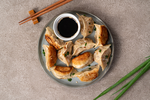 Taiwanese and Japanese Pan-fried gyoza dumpling jiaozi food in a plate with soy sauce on gray table background.