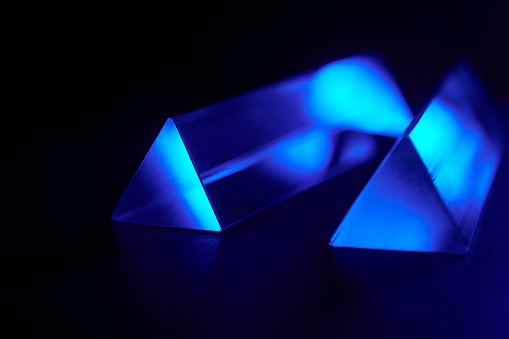 Close up of crystal triangular prism optical glass with blue light spectrum abstract background