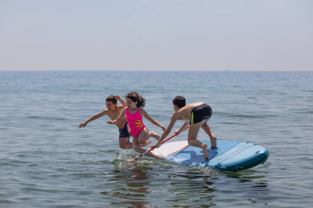 istock Three kids falling off a paddle surf on a summer day 1404154250