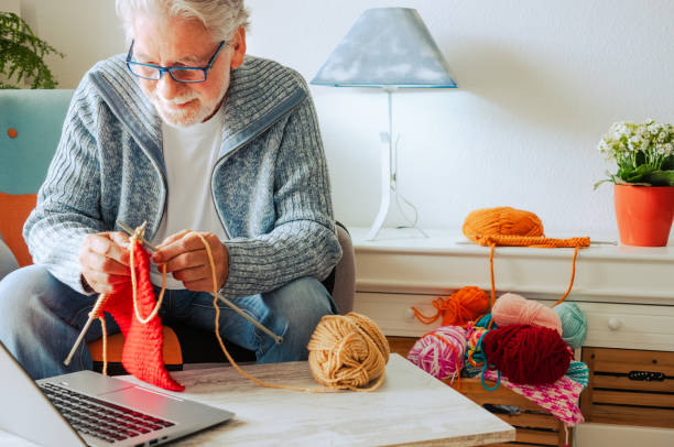 istock Senior man at home follow online knit tutorial to relax and enjoy resting home leisure activity sitting on the sofa - male people knitting with computer class help - people inner lifestyle hobby 1404156014