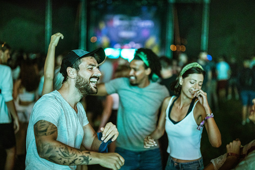 Cheerful man having fun while dancing on a music festival during night with his friends.