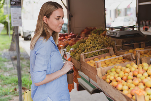 young charming woman chooses fruits at street shop