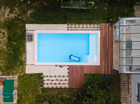 Drone flight over beautiful green garden with pool and the wooden terrace of the pool is currently in progress