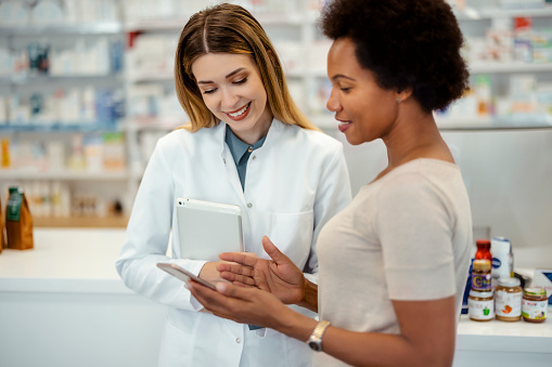Pharmacy Drugstore: African American Female Customer Showing Mobile Phone to Young Female Chemist in Pharmacy
