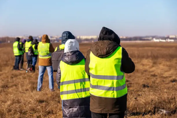 Group of many people watching planes landing and take off airport runway field planespotting conference warm morning time. Planespotters in safety vest waiting aicraft arrival approaching departure.