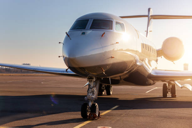 scenic front view modern luxury expensive private jet plane parked airport taxiway hangar warm colorful dramatic evening warm sunset sun light sky background. executive aicraft vip travel concept - corporate jet imagens e fotografias de stock