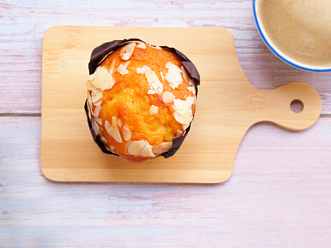 Freshly baked homemade almond muffins in brown paper cup on wooden chopping board and coffee cup over rustic table. Top view, flat lay and space for your text.