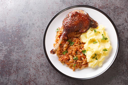 Romanian food duck leg with stewed cabbage and mashed potatoes close-up in a plate on the table. horizontal top view from above
