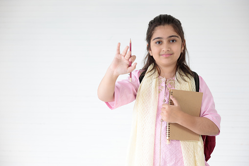 cute Indian girl showing pencil and holding notebook for learning, education concept