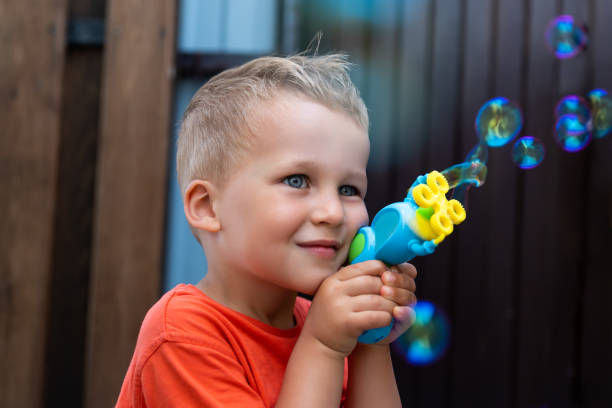 nahes porträt eines niedlichen kleinen bond-kind-jungen genießen sie es, seifenblasen im haushof im freien an hellen, warmen sommertagen gegen die hauswand zu blasen. kinder gesund außerhalb der natur aktivitäten - child bubble wand children only park stock-fotos und bilder