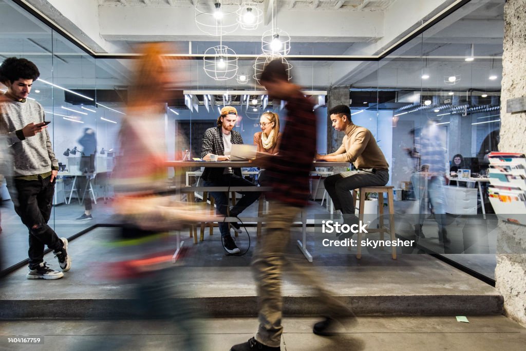 Young creative people working in the office among people in blurred motion. Group of young freelancers working on wireless technology at casual office. Some people are in blurred motion. Technology Stock Photo