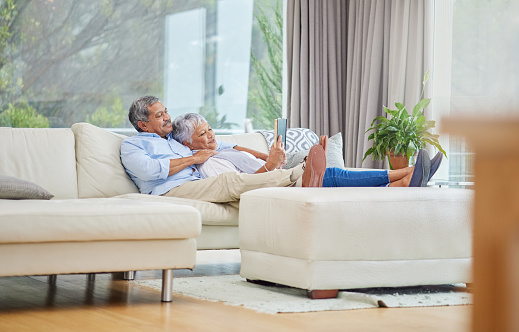 Closeup of an affectionate mixed race senior couple relaxing and reading a book in their living room at home. Hispanic man and wife  bonding on the sofa in the living room being affectionate