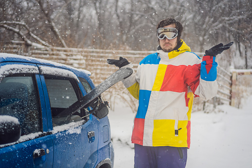 The snowboard does not fit into the car. A snowboarder is trying to stick a snowboard into a car. Humor, fun.