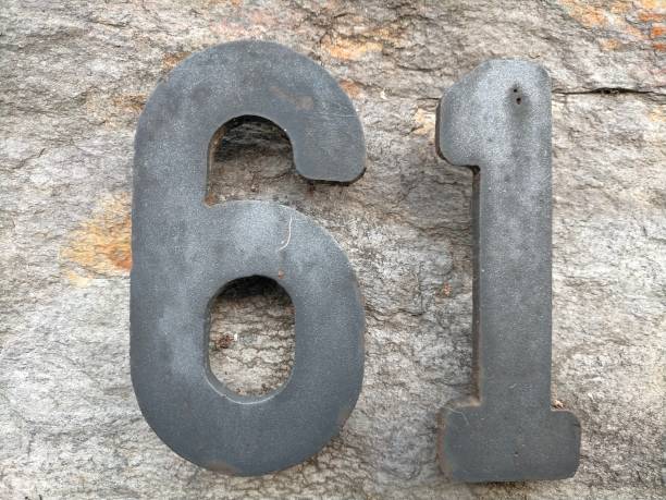 istock 61, number sixty-one in dark colored metal,on a stone wall 1404173924