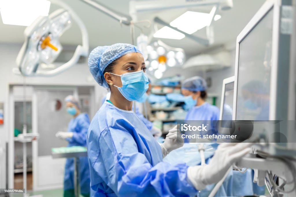 Anesthetist Working In Operating Theatre Wearing Protecive Gear checking monitors while sedating patient before surgical procedure in hospital - Royalty-free Profissional de enfermagem Foto de stock Anesthetist Working In Operating Theatre Wearing Protecive Gear checking monitors while sedating patient before surgical procedure in hospital - Royalty-free Profissional de enfermagem Foto de stock