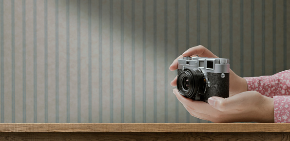 Woman holding a vintage camera and retro wallpaper in the background, creativity and hobbies concept