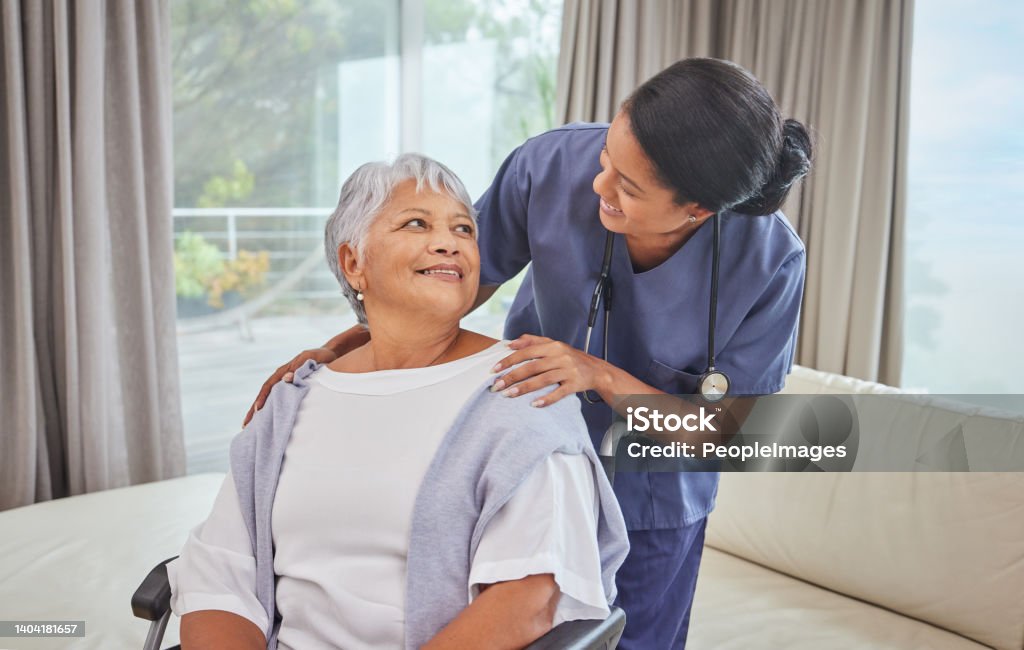 A hispanic senior woman in a wheelchair and her female nurse in the old age home. Mixed race young nurse and her patient in the lounge Senior Adult Stock Photo