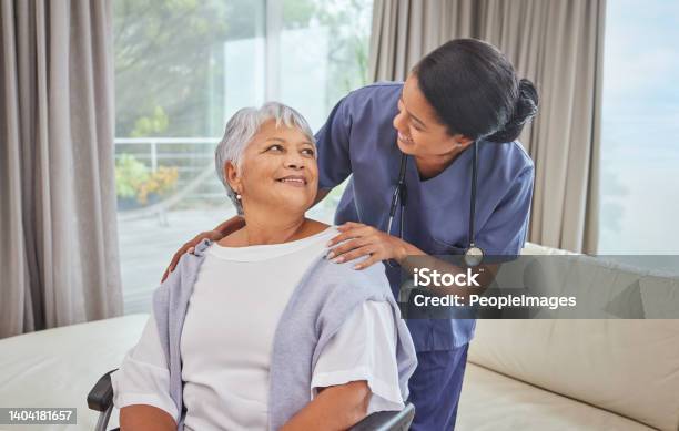 A Hispanic Senior Woman In A Wheelchair And Her Female Nurse In The Old Age Home Mixed Race Young Nurse And Her Patient In The Lounge Stock Photo - Download Image Now