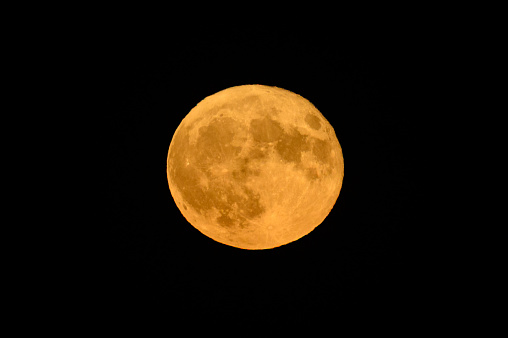 Full moon, supermoon, or springtime strawberry supermoon in the spring night with clearly visible moon surface in the dark night sky over Kampen, Overijssel, Netherlands. Shot with a long telelens.