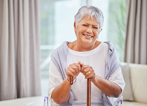 Portrait of a senior hispanic woman leaning in her walking stick at home. Mixed race female sitting on a sofa  relaxing while holding a walking cane