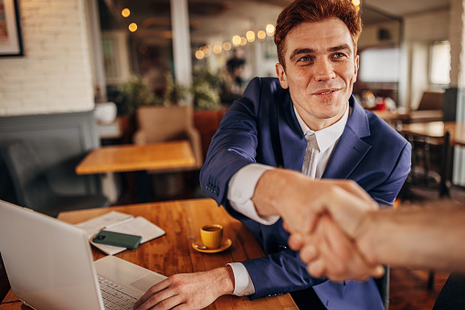 Portrait of a handsome young businessman shaking hands with another person in cafe.