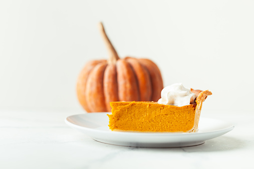 Cut slice of pumpkin pie close up on white background. Autumn orange cake
