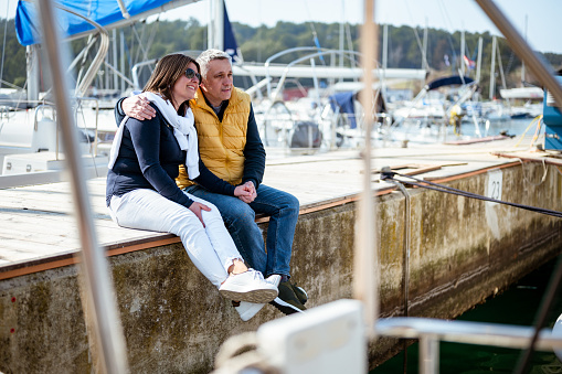 Adult mature couple sittin on a concrete pier in a port.