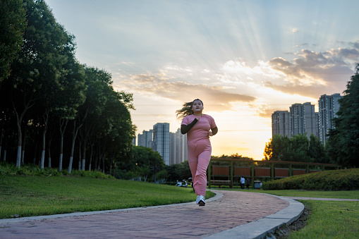 A plump young asian woman, wearing sportswear, was running in the park. Exercise to lose weight.