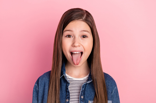 Photo portrait of wearing jeans jacket little girl grimacing showing tongue isolated on pastel pink color background.