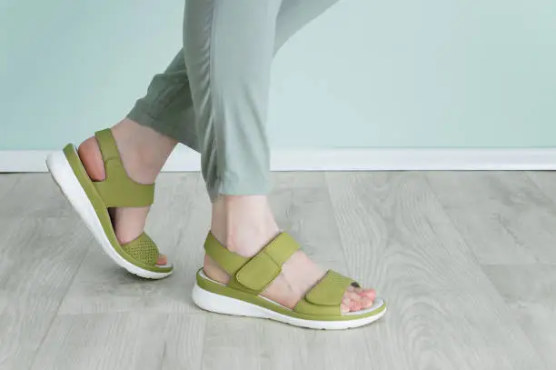 Legs of a caucasian woman in green trousers and Velcro sandals.