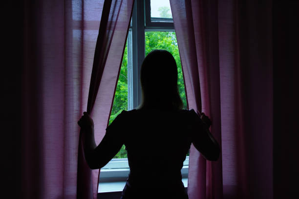istock Woman at  window with curtains at dawn. View from the back. 1404191278