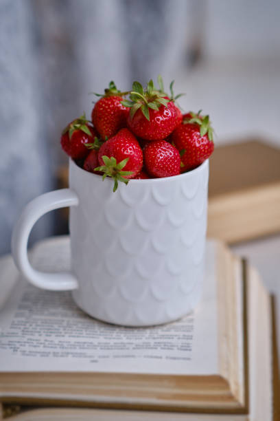 istock Mug filled with fresh strawberries and book. Selective focus. 1404191589