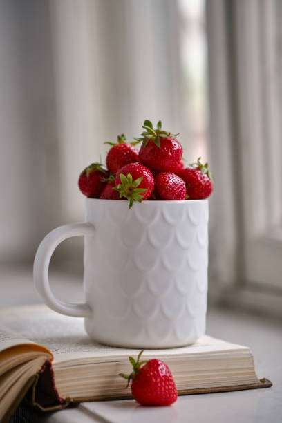 istock Mug filled with fresh strawberries and book. Selective focus. 1404191605