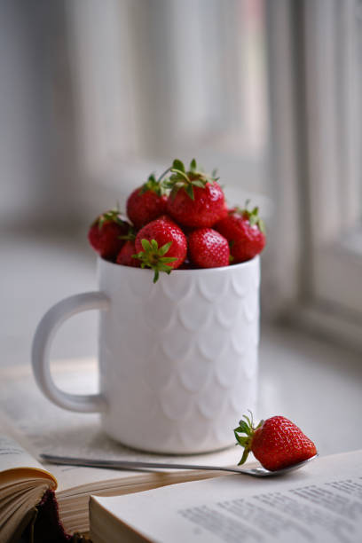 istock Mug filled with fresh strawberries and book. Selective focus. 1404191614