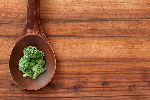 Top view of wooden spoon over table with raw broccoli on it