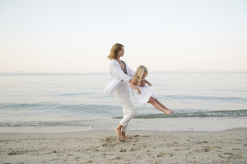 Mother and daughter having fun on the beach. Mother holding girls hands and spinning around. Family outdoor activities concept.