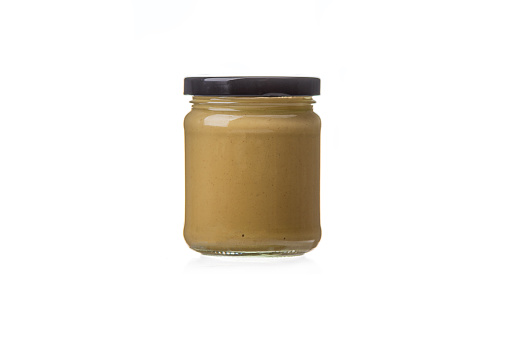 Closed glass jar with Dijon mustard on a white background. Black lid, copy space.