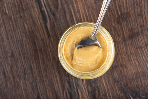 Top view of Dijon mustard in a jar and a spoon inside it. Copy space.