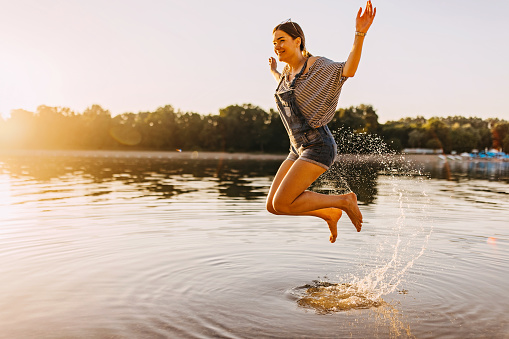 A young Caucasian woman is having fun in the water, jumping up and down cheerfully.